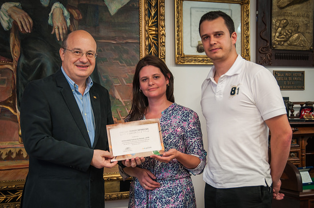 Rafael e Antoniella, do Instituto GRPCOM, entregaram, o certificado ao reitor. Imagem: Samira Chami Neves. 